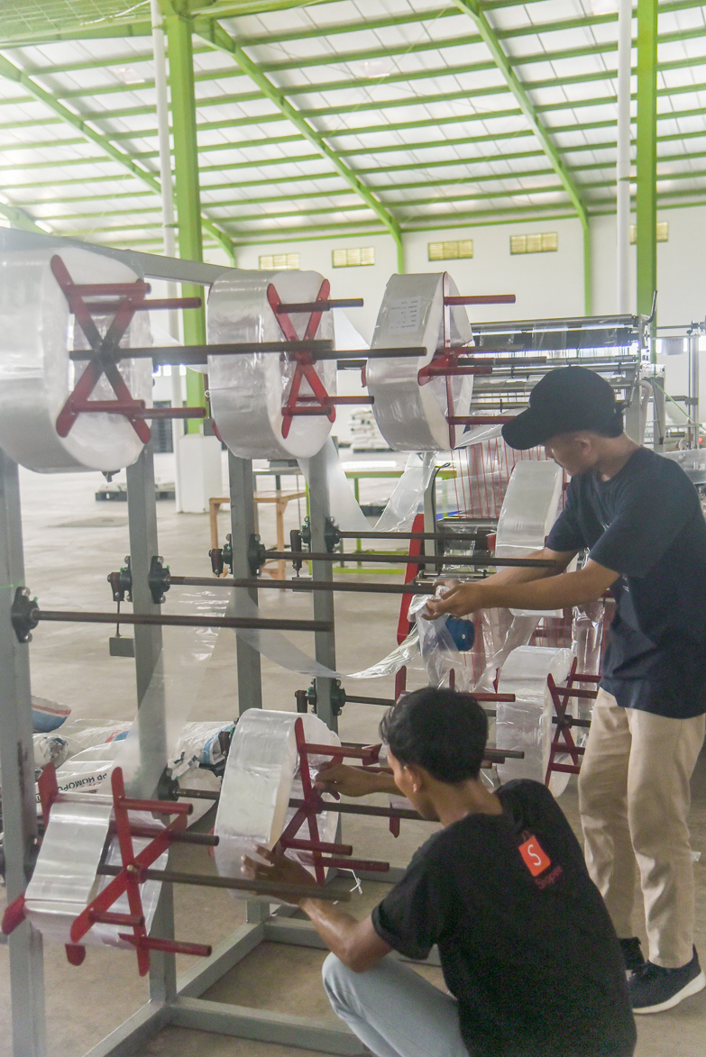 Persons repairing heavy machinery in a plastic manufacturing factory in Indonesia